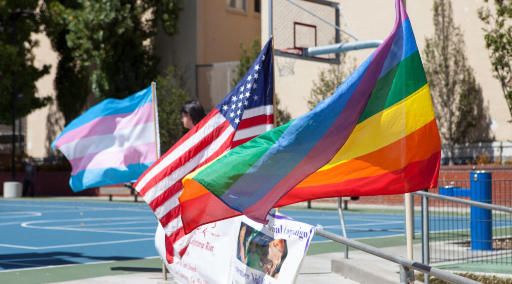 Flags representing LGBT pride, the USA, and trans pride flying outdoors at a park in San Francisco