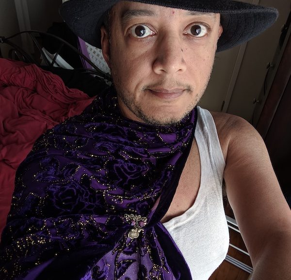 Pax with black hat, white tank top, and purple cape