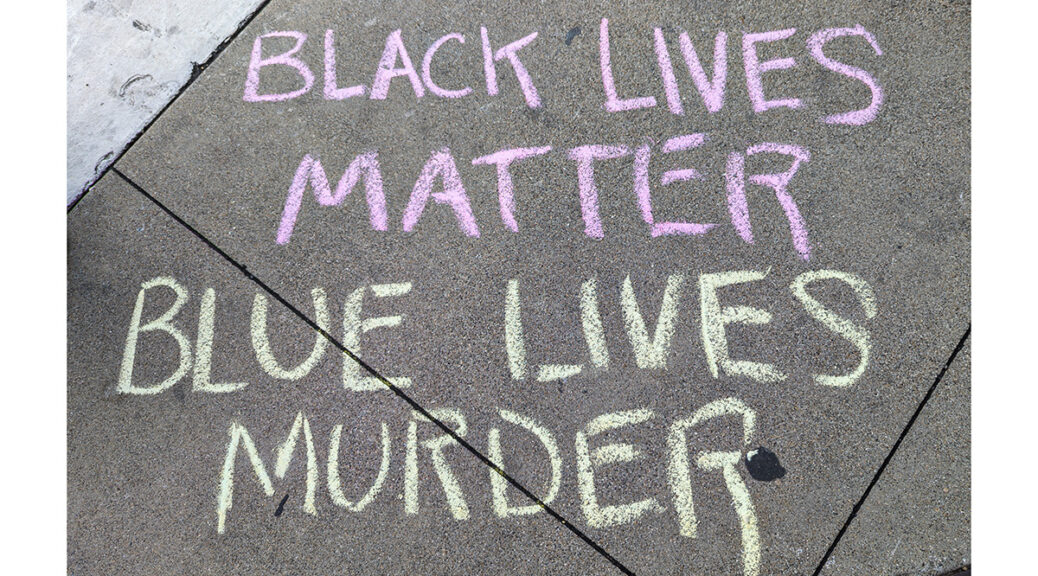 A chalked message on the sidewalk reads “BLACK LIVES MATTER BLUE LIVES MURDER”.