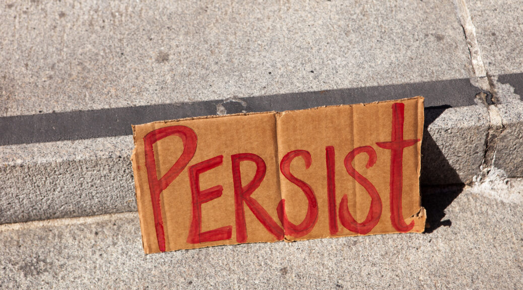 A cardboard sign reading “Persist” sits on concrete steps.