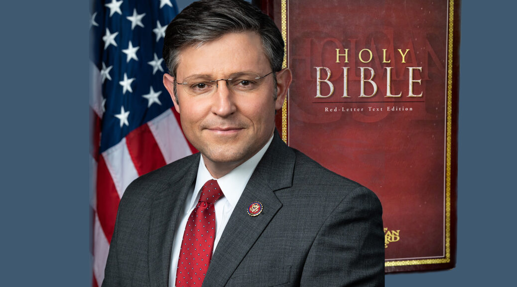 Mike Johnson smiles slightly while looking into the camera. He is standing in front of an American flag and wearing a dark gray jacket, red tie, and glasses. Superimposed behind him is a photo of a Bible in dark brown with gold trim, and the words “Holy Bible — Red-Letter Text Edition”.
