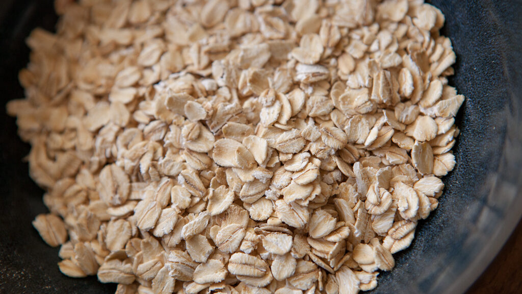 Top-down, close-up view of old-fashioned rolled oats in a dark blue bowl.