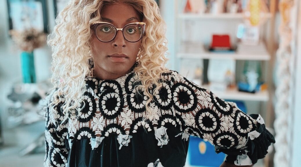 Aria Sa'id, a Black woman with long curly hair and glasses, looks into the camera.